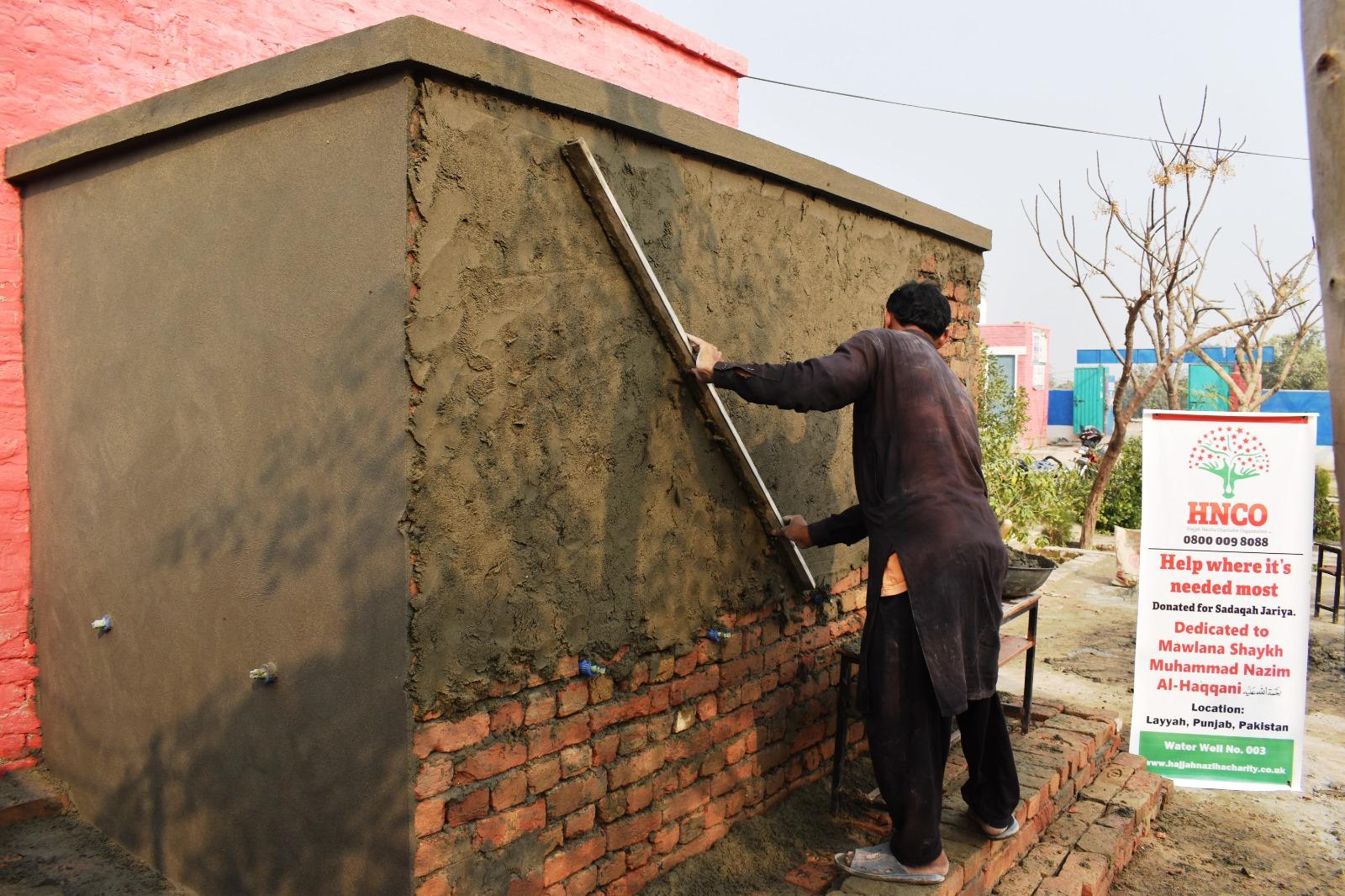 Worker plastering pump house walls at water well site